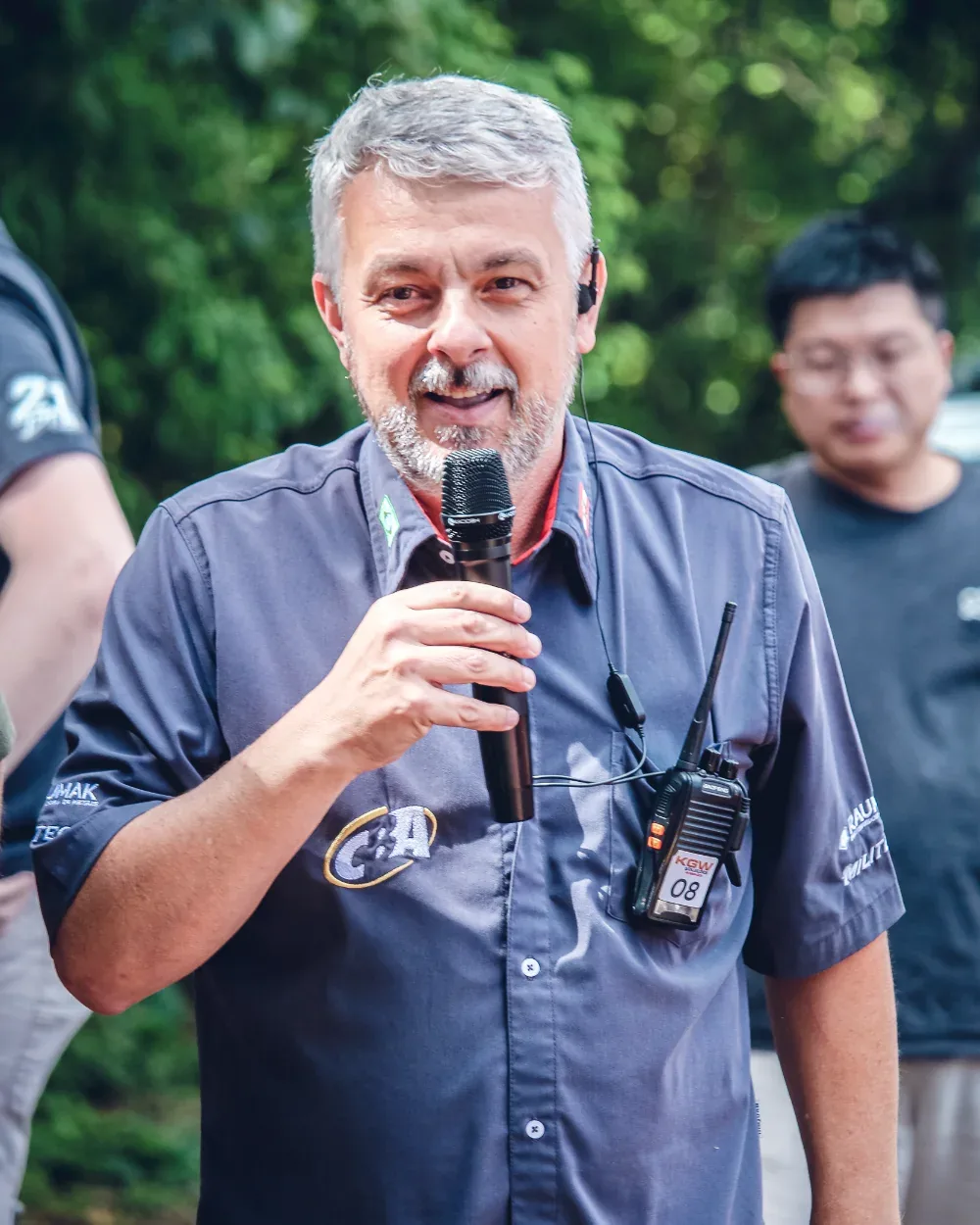 Fabio Chiarello falando ao microfone, com rádio comunicador no bolso, durante um evento de arrancada